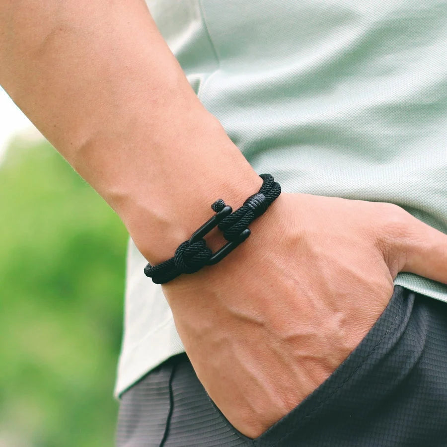 Person wearing a black braided bracelet on a blurred green background
