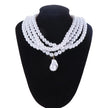 a choker-style necklace made of four rows of small, round white pearls. It has a gold-toned clasp at the back and a single, larger, teardrop-shaped white pearl pendant hanging from the center front, on a black mannequin bust with a white background