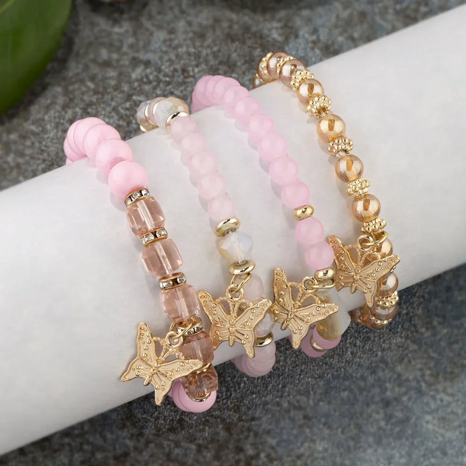 Set of pink beaded bracelets with gold butterfly charms on a wrist.