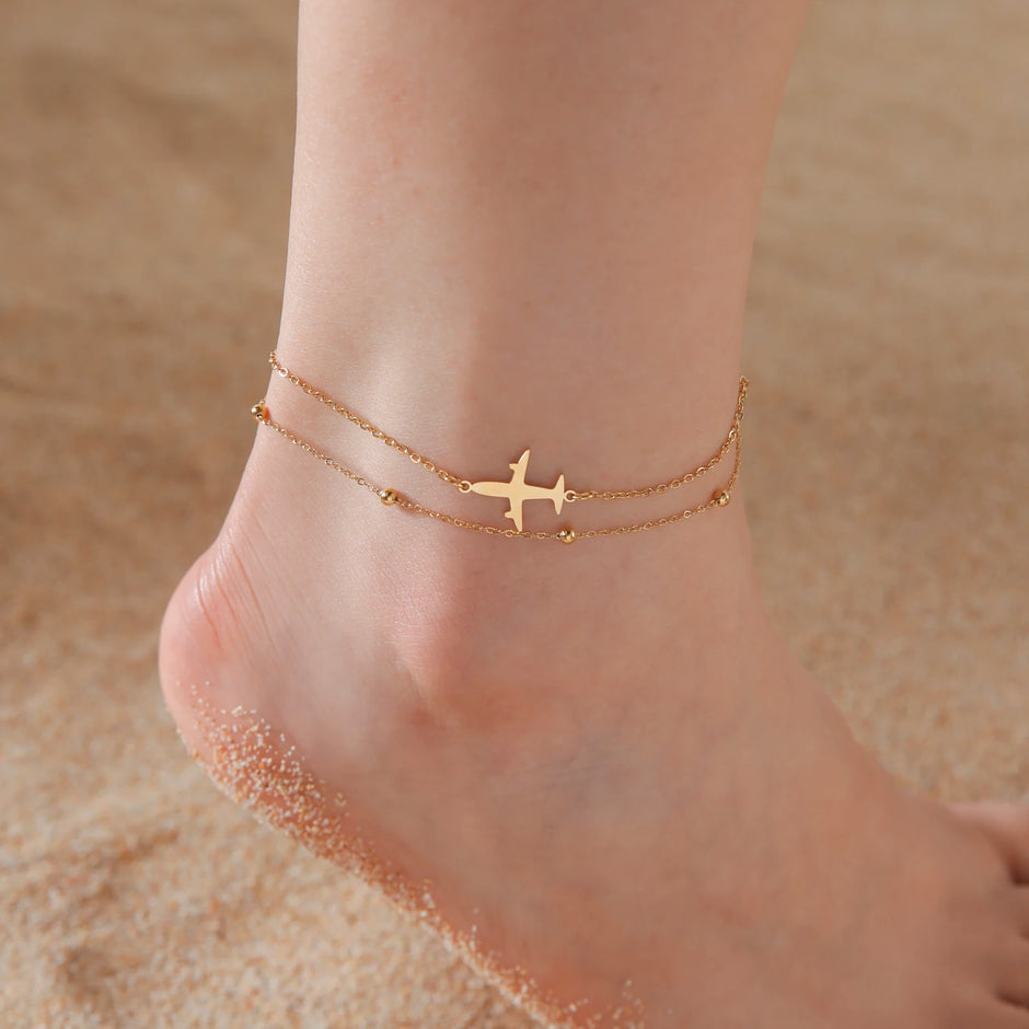Gold airplane anklet on a foot with sand background