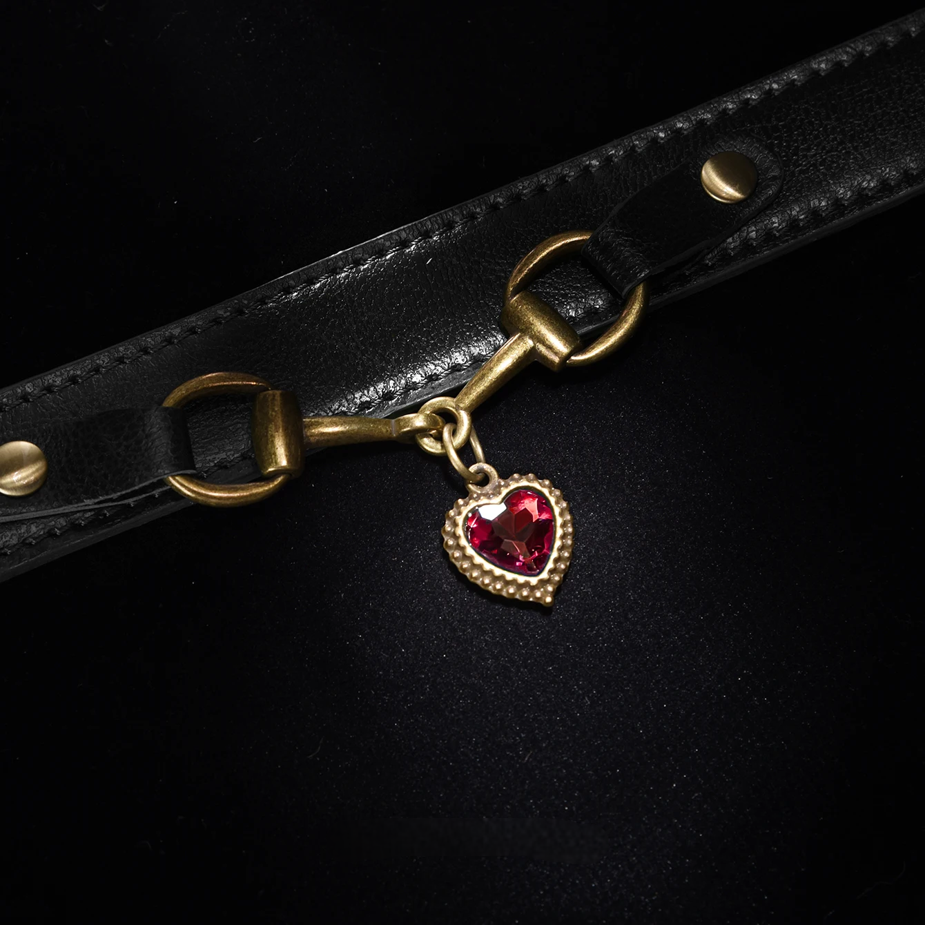 Black leather strap with gold hardware and a red heart charm on a black background
