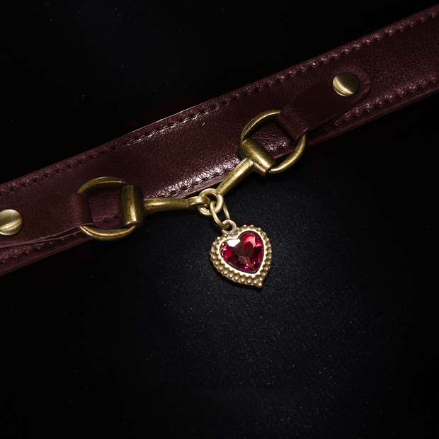 Brown leather strap with a gold buckle and red heart charm on a black background