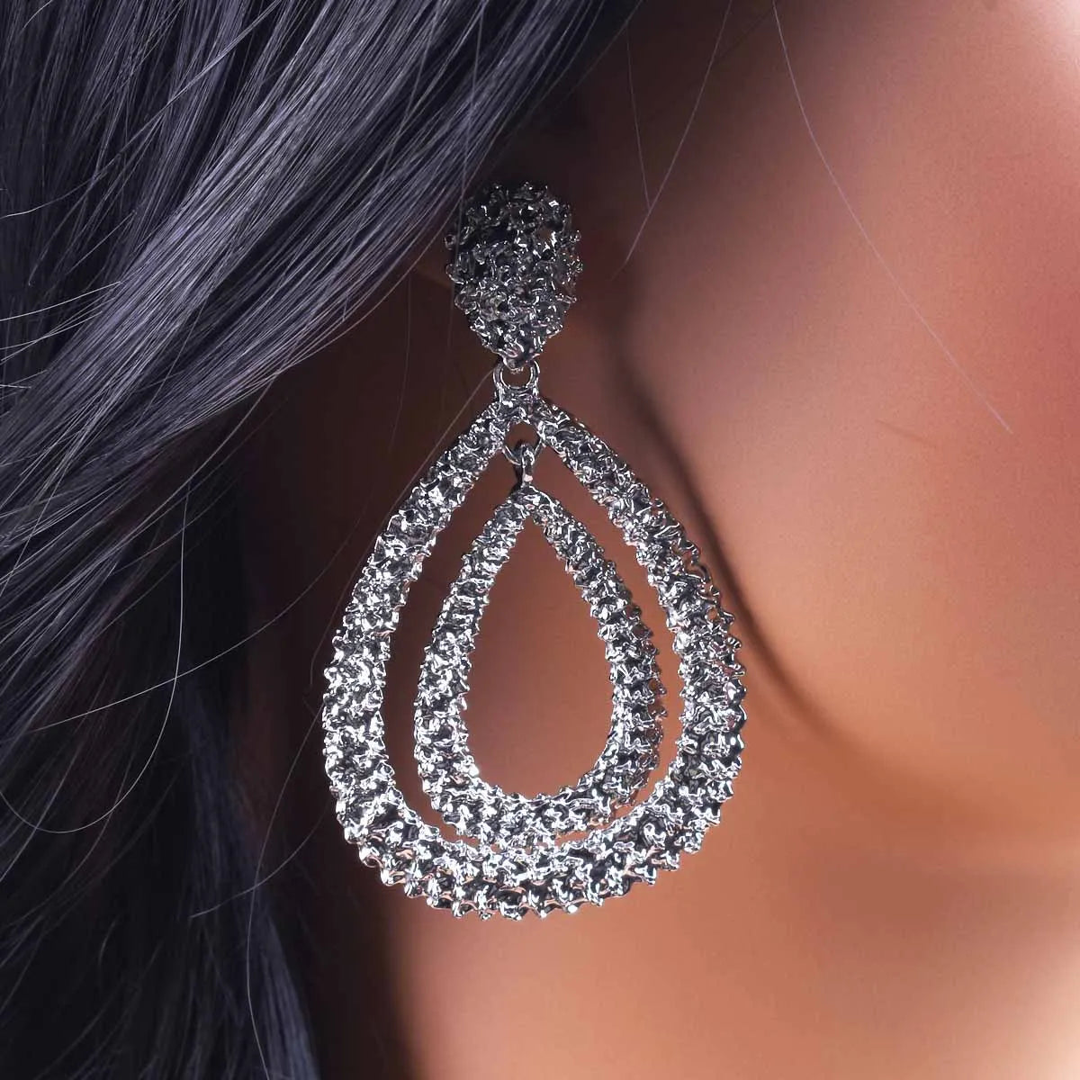 Silver teardrop earring worn by a person with dark hair.
