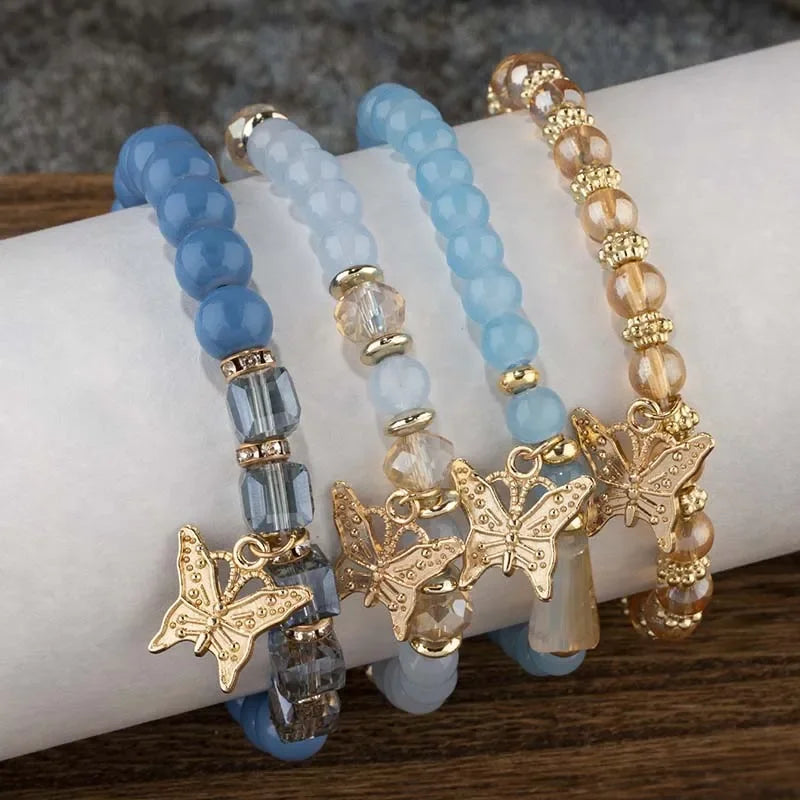 Set of  blue beaded bracelets with butterfly charms on a wrist against a neutral background