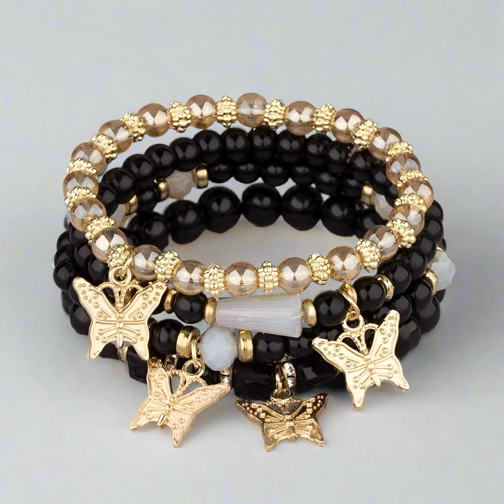 Stack of black beaded bracelets with butterfly charms on a textured surface