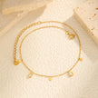 Gold anklet with heart and round charm on a beige surface