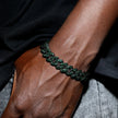 Close-up of a hand wearing a green braided bracelet on a dark background