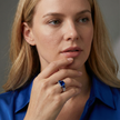 Woman wearing a blue ring with a large gemstone, wearing a blue shirt against a neutral background