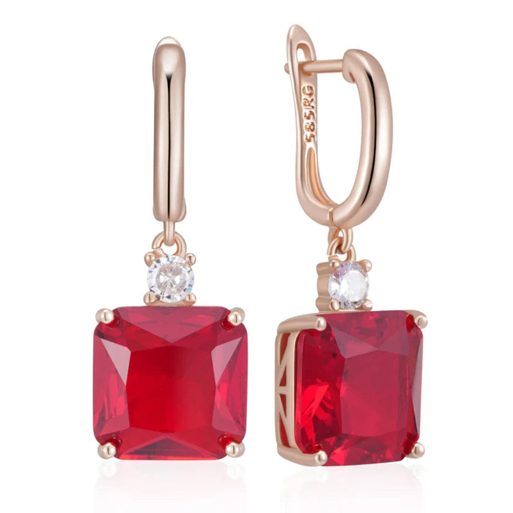 Rose gold earrings with red gemstones on a white background