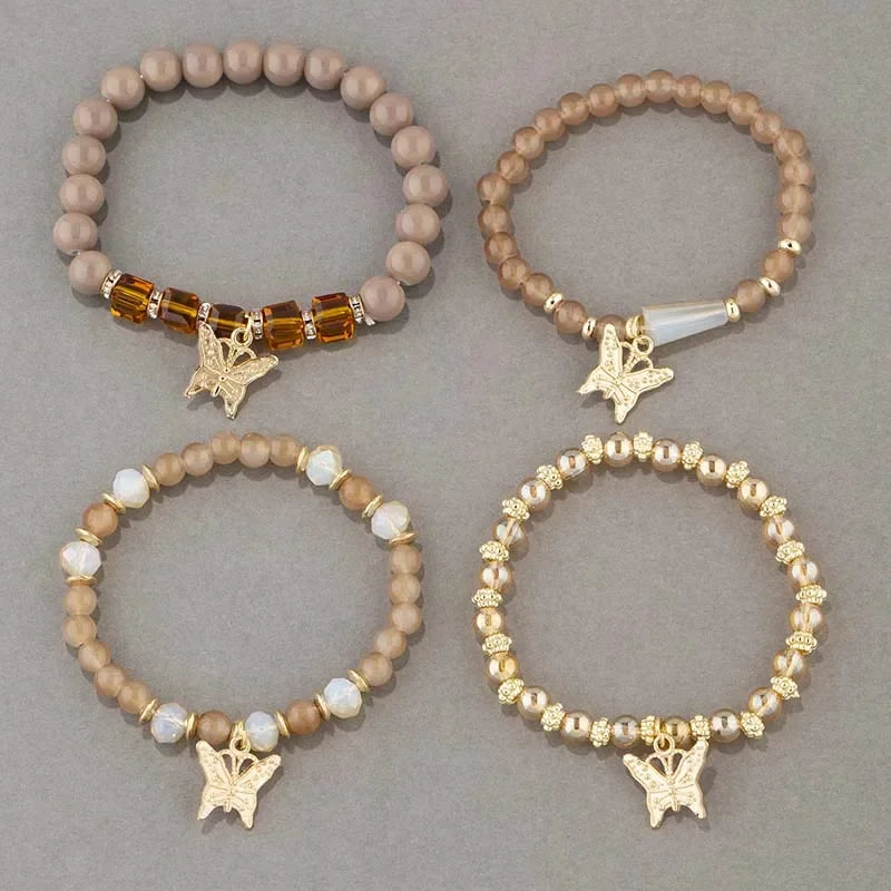 Four beaded bracelets with butterfly charms on a gray background