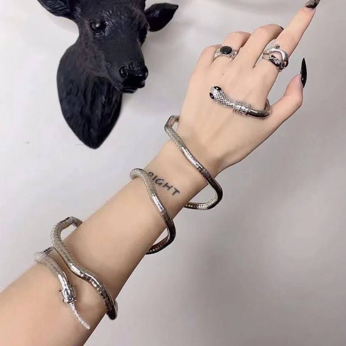 Hand wearing multiple silver rings and bracelets with a black sculpture in the background