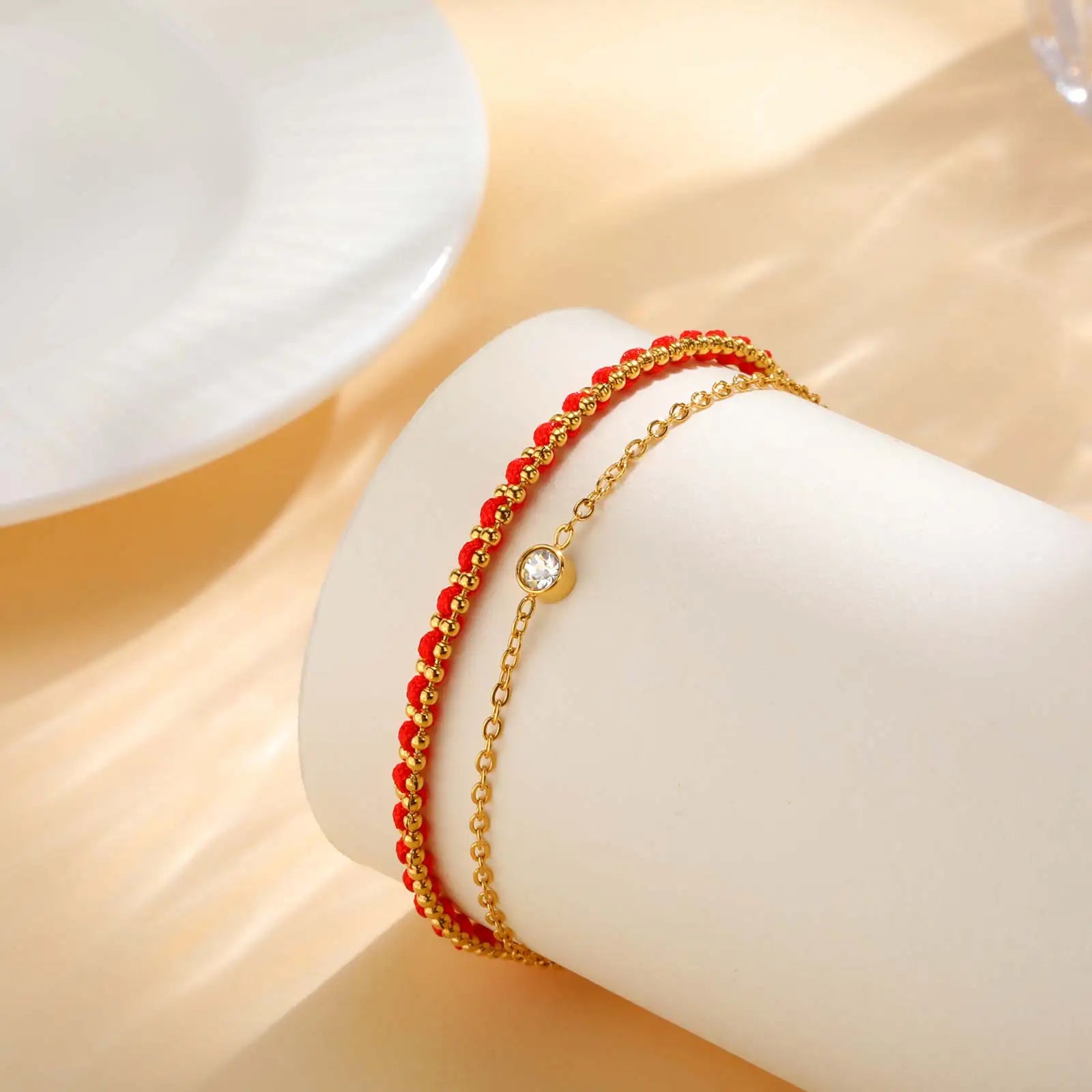 Gold and red beaded bracelet on a white cylindrical holder with a soft beige background