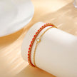 Gold and red beaded bracelet on a white cylindrical holder with a soft beige background