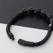 Black braided bracelet with metal clasp on a white surface
