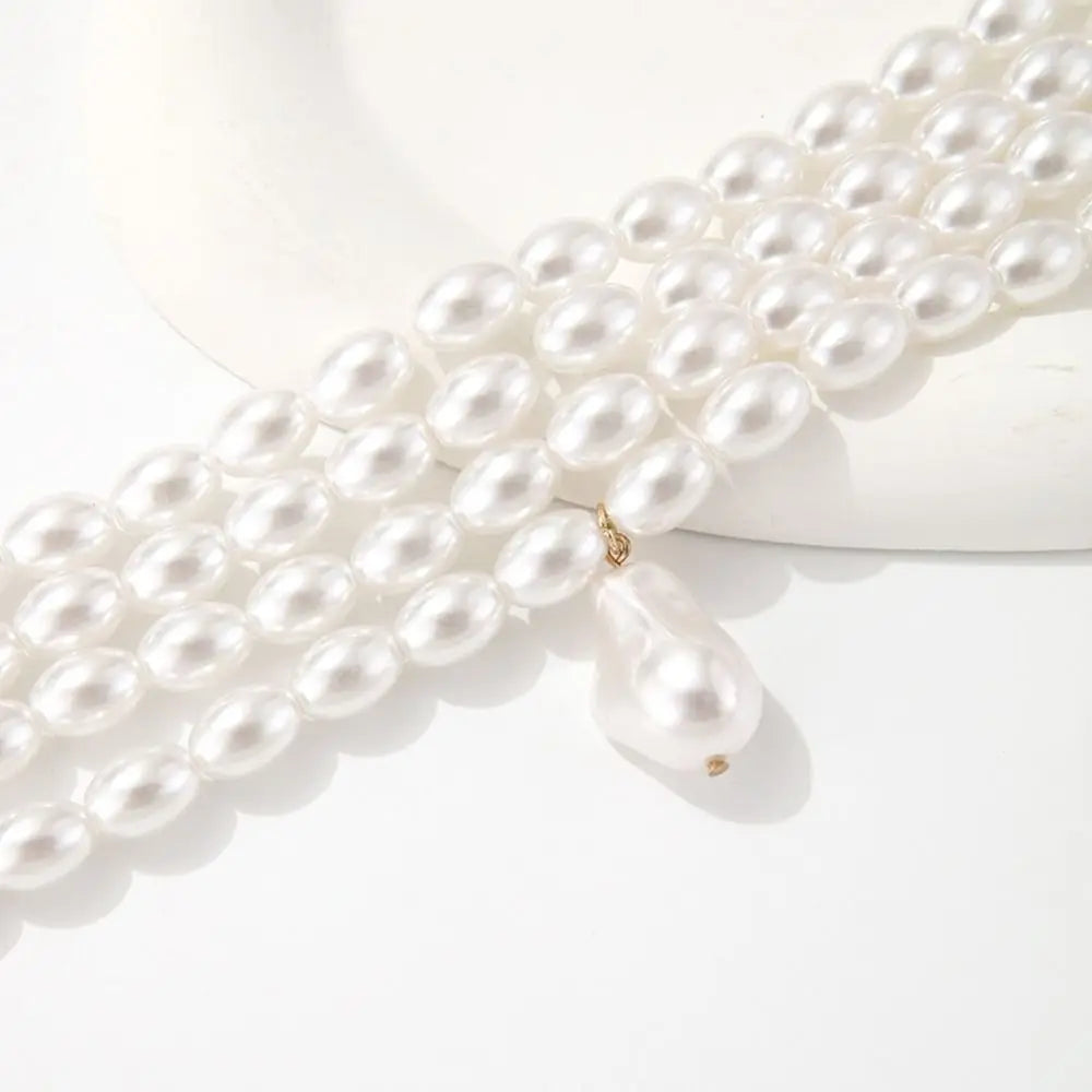 A four-layered white baroque pearl choker necklace with a gold-tone clasp and a single large, irregular baroque pearl dangling from the center.