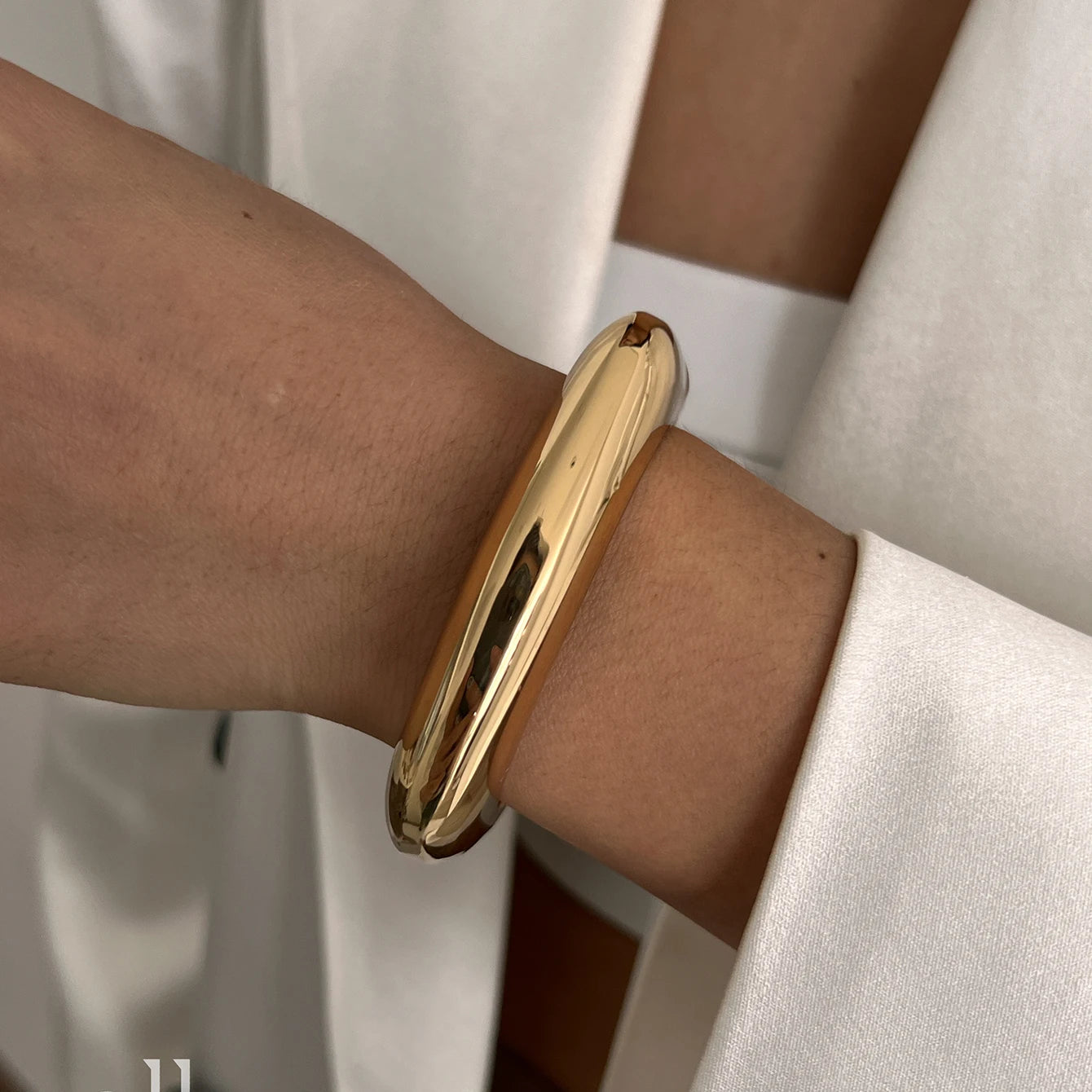 Gold bracelet on a wrist with a neutral background