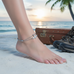 Foot with anklet on sandy beach with suitcase and boots in background