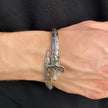 Silver bracelet with sword design on a wrist against a black background