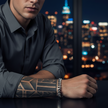 Man with tattooed arm and bracelet sitting in front of a cityscape at night