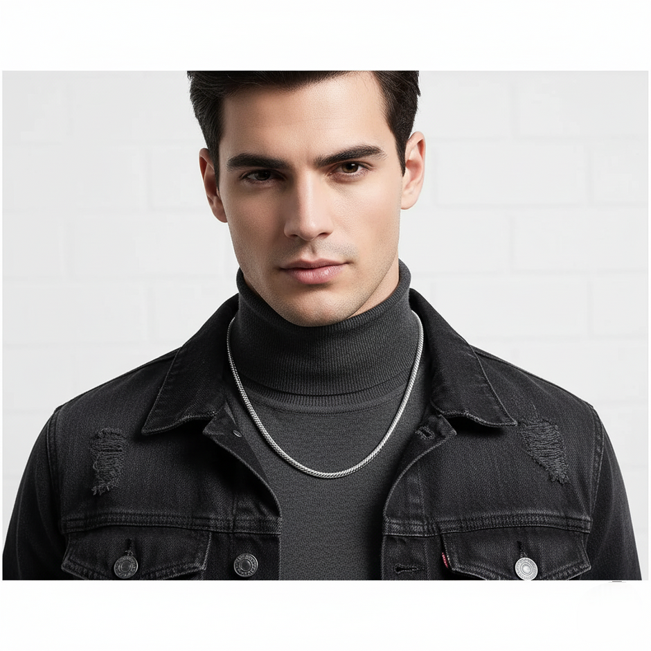 Man wearing a black denim jacket and gray turtleneck with a silver chain necklace on a light gray background