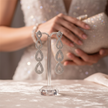 Silver earrings on a stand with a blurred background of a person holding a clutch.