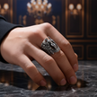 Hand wearing a silver winged ring on a dark surface with a blurred background