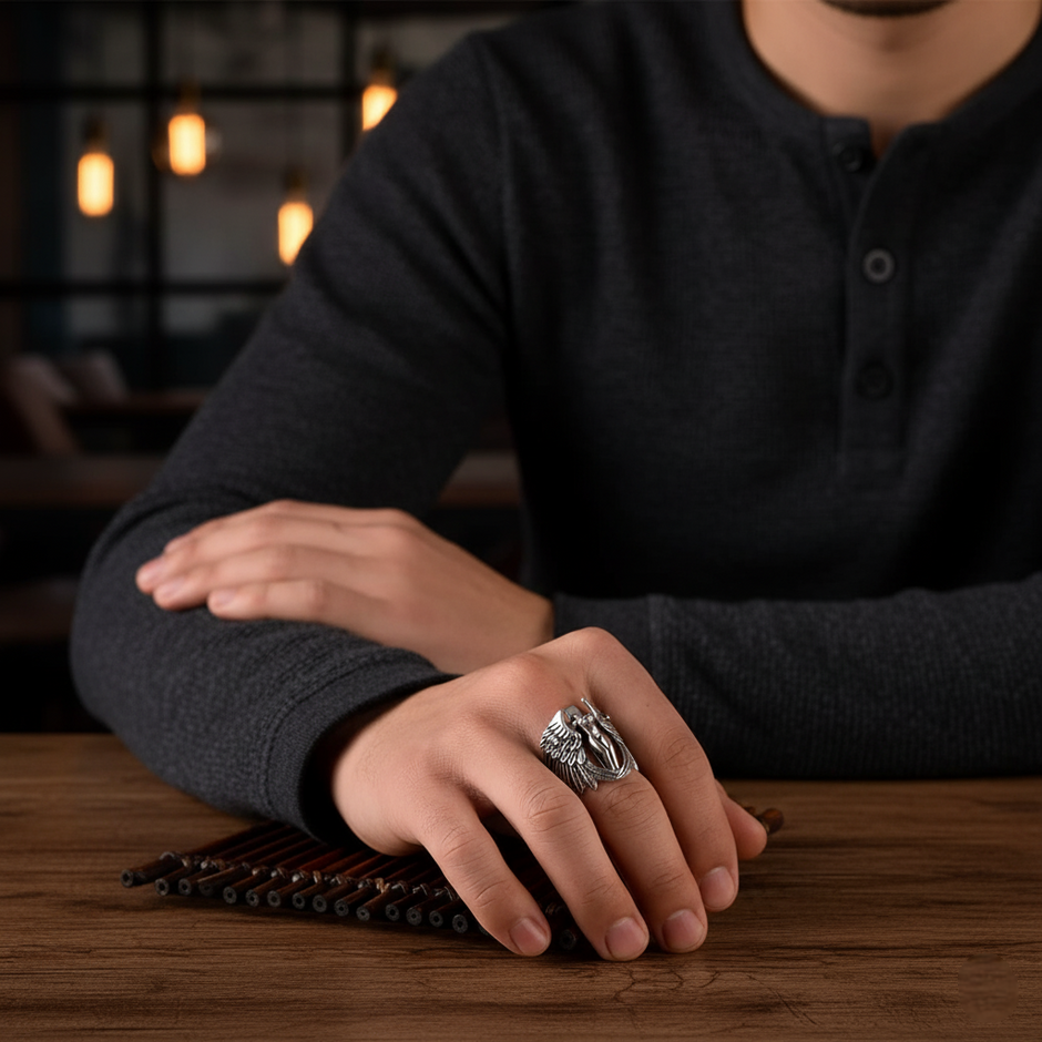 Person wearing a dark shirt with a Silver ring with angel design on a wooden surface