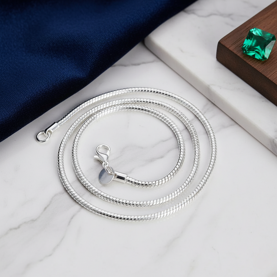Silver snake chain necklace on a marble surface with a green gemstone in the background