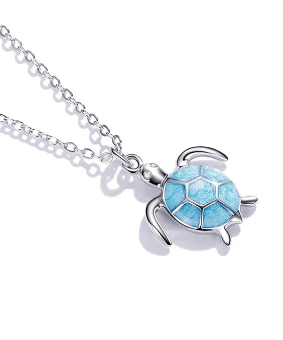 Silver turtle pendant with a blue gem on a white background