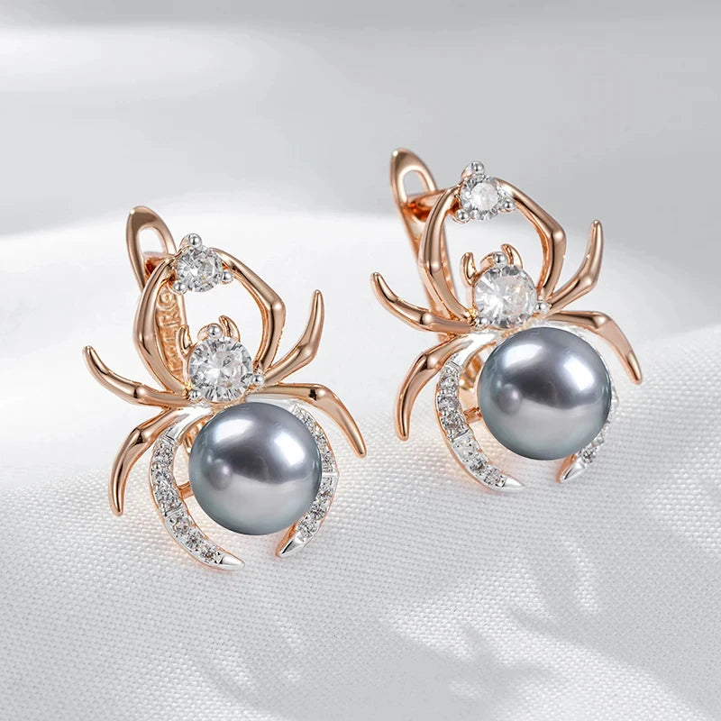 Spider-shaped earrings with gray pearls and rose gold accents on a white fabric background