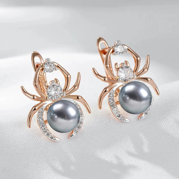 Spider-shaped earrings with gray pearls and rose gold accents on a white fabric background
