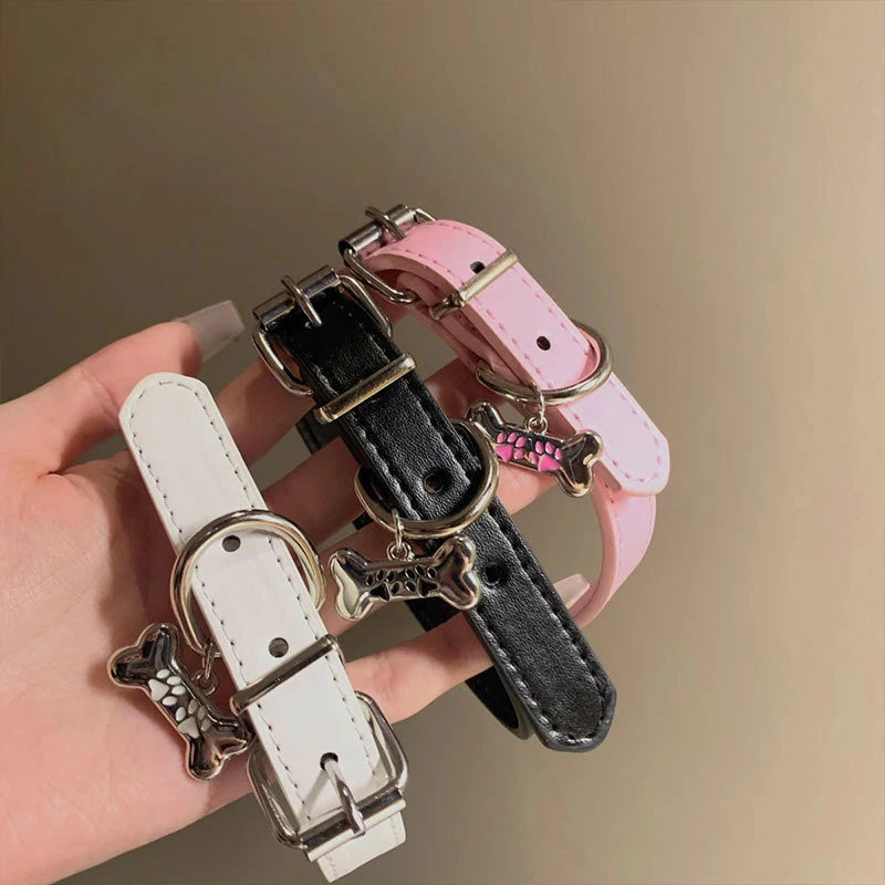Three dog collars in white, black, and pink are held by a hand against a beige background.