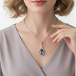 Woman wearing a necklace with a blue pendant, pointing to it.