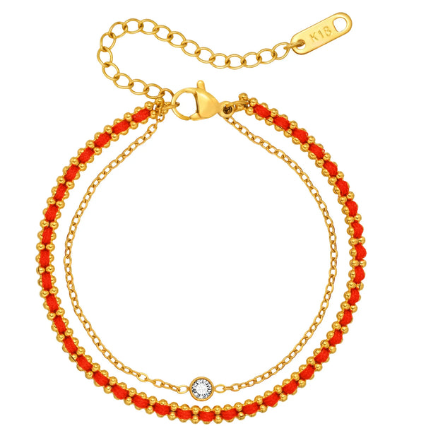 Two gold bracelets with red beads on a white background