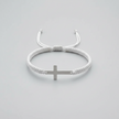 White braided bracelet with a silver cross charm on a light gray background