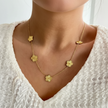  a gold necklace with multiple golden clover-shaped links. worn by a person against a neutral background