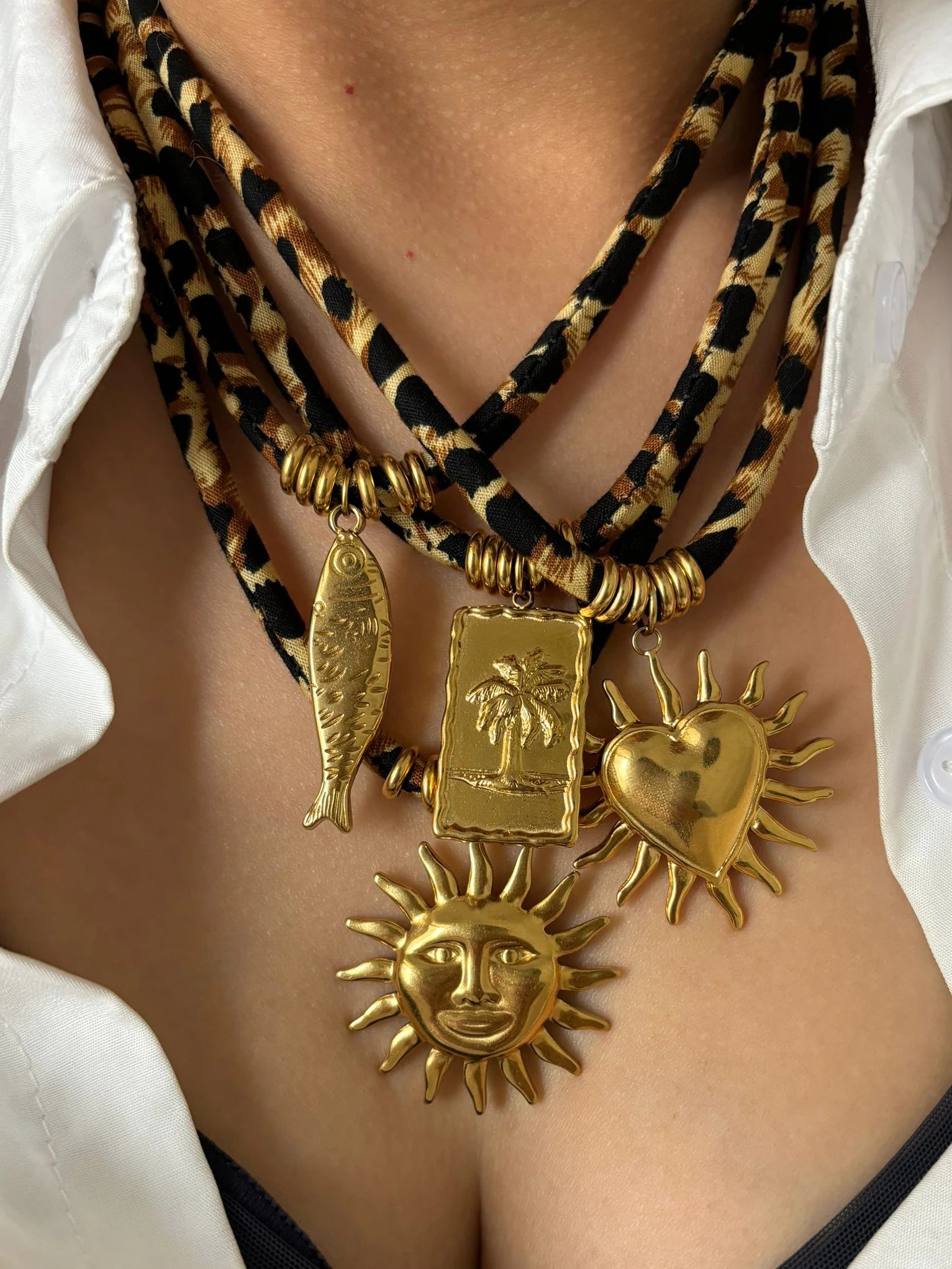 Necklace with gold pendants including a sun, heart, and fish on a white shirt background