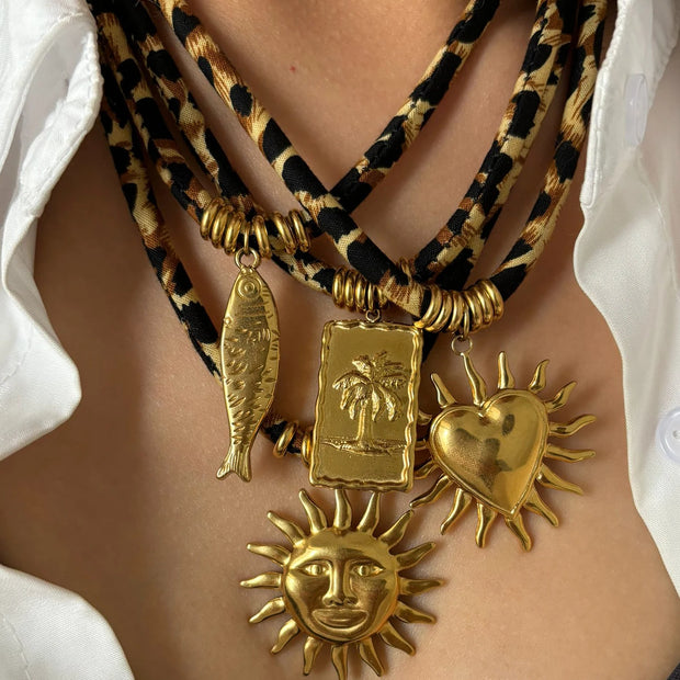 Necklace with gold pendants including a sun, heart, and fish on a white shirt background