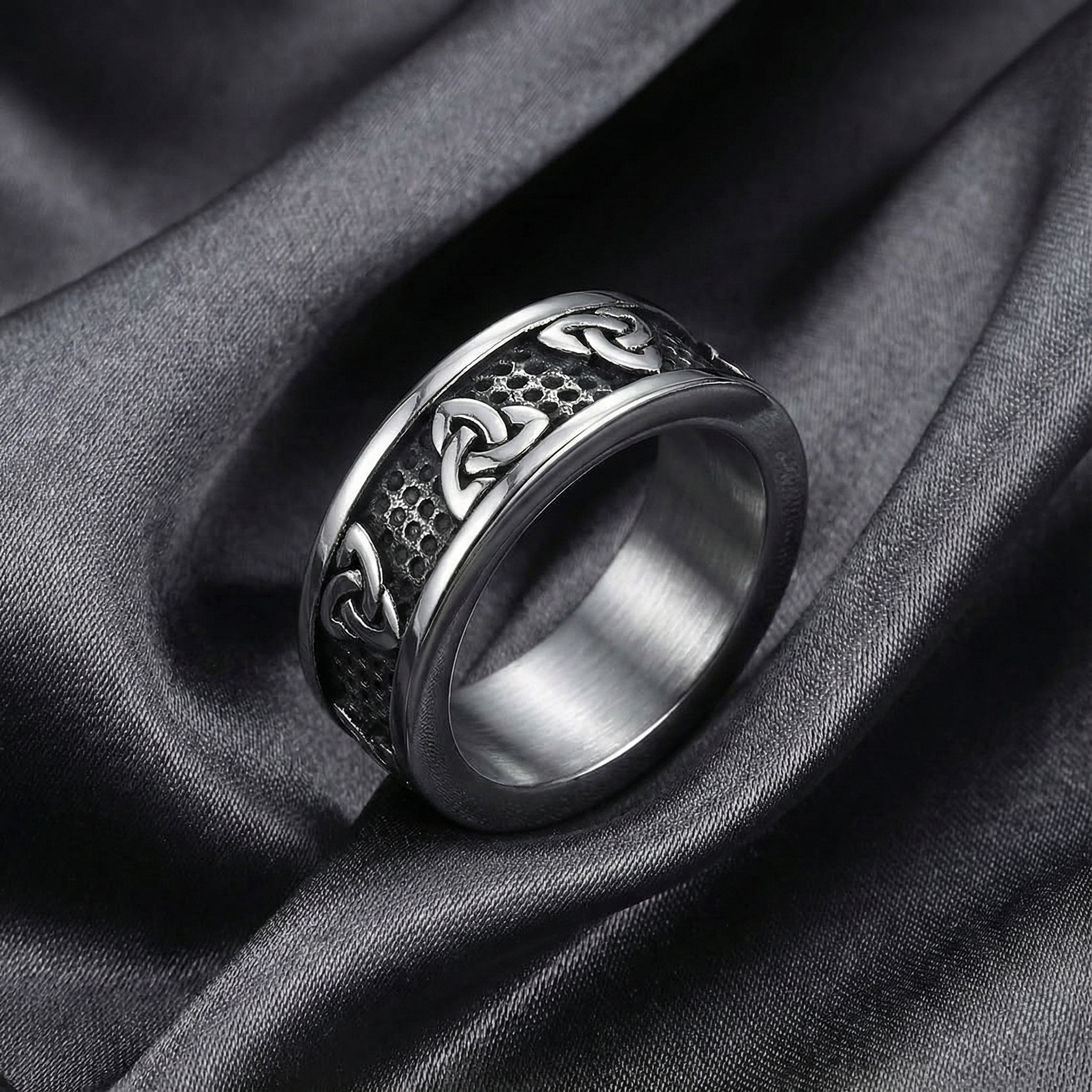 Silver ring with intricate design on a dark fabric background