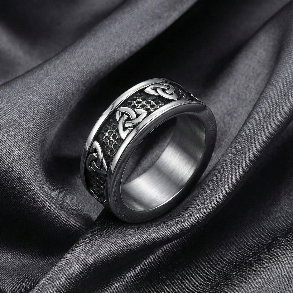 Silver ring with intricate design on a dark fabric background