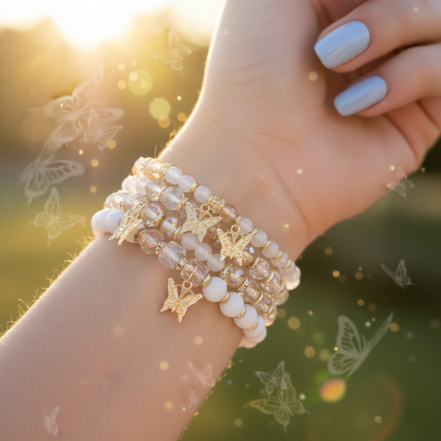 Hand wearing multiple bracelets with butterfly charms against a blurred natural background