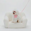 White dog with a pink bow sitting on a white bean bag chair against a white background