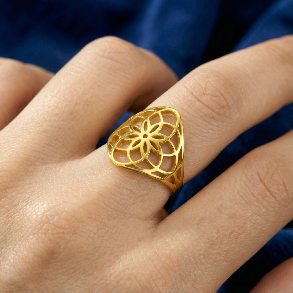 Flower of life Gold ring with intricate design worn on a finger against a blue fabric background