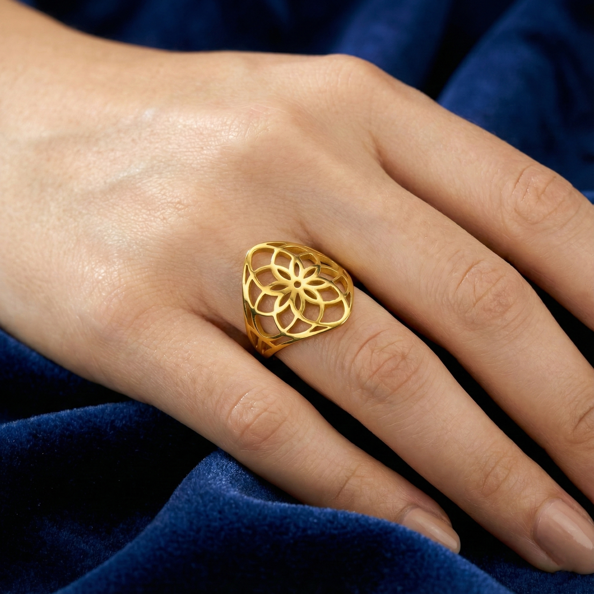 flower of life Gold ring with a intricate design on a person's finger against a blue fabric background
