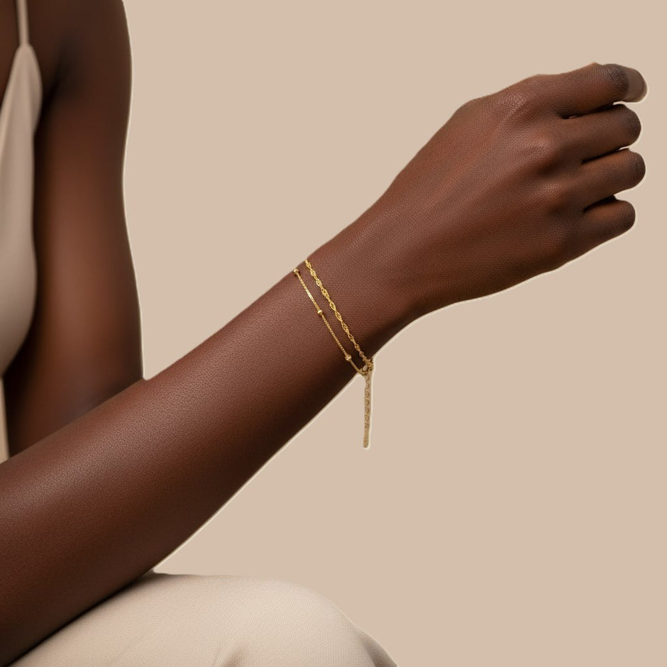 Gold bracelet on a person's wrist against a beige background