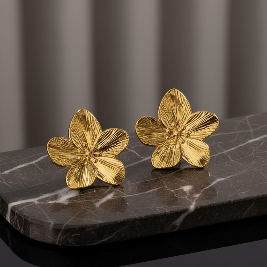 Gold flower-shaped earrings on a dark marble surface