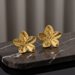 Gold flower-shaped earrings on a dark marble surface