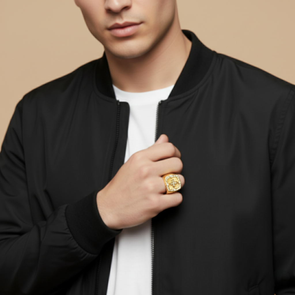 Man wearing a black jacket with a gold ring on his hand against a beige background