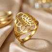 Gold stainless steel ring with intricate design on a beige fabric background