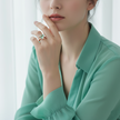 Woman wearing a green blouse with a ring on her finger against a white background